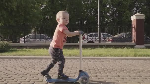 Un niño encantador en el patinete scooter del parque. Movimiento lento — Vídeo de stock