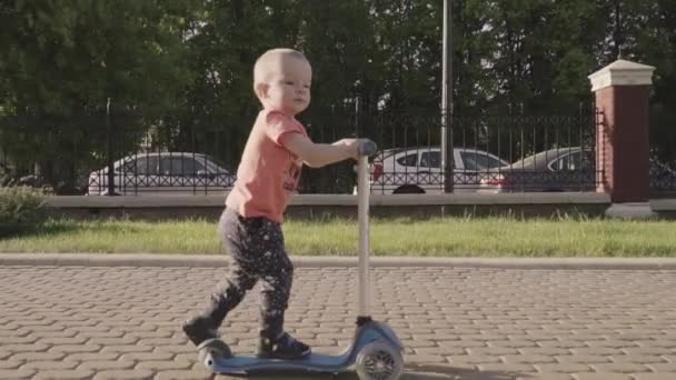 Lite härlig pojke på kick skoter i parken. Slow motion — Stockvideo