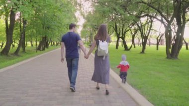 Güzel aile zevk yaz günü parkta: annem ve babam ilk adımlarını yapmak için ona yardım ile yürümeyi öğrenen küçük bebek