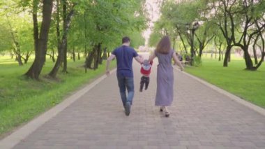 Güzel aile zevk yaz günü parkta: annem ve babam ilk adımlarını yapmak için ona yardım ile yürümeyi öğrenen küçük bebek