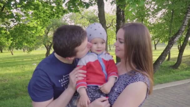 Feliz jóvenes padres compartir beso su lindo bebé chico al aire libre en parque — Vídeo de stock