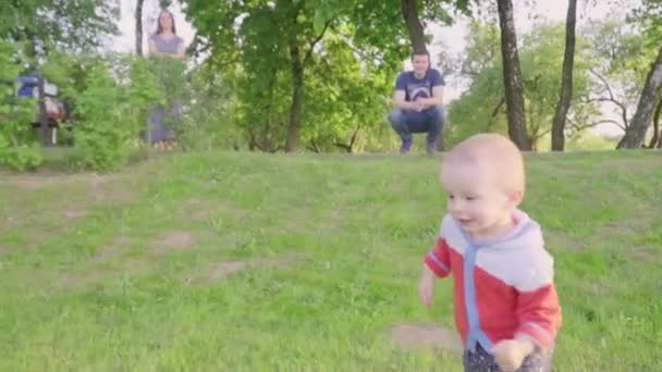 Glückliches kleines Kind spielt mit seinen Eltern im Park auf dem Rasen im Sonnenlicht — Stockvideo