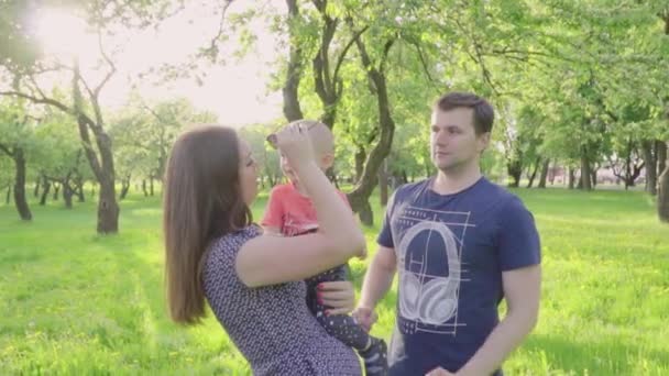 Jovens pais felizes compartilhar beijar seu menino bonito ao ar livre no parque. Movimento lento — Vídeo de Stock