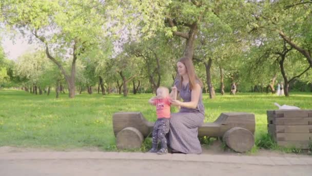 Yong hermosa mujer con su pequeño sol sentarse en el banco en el parque. Movimiento lento — Vídeos de Stock