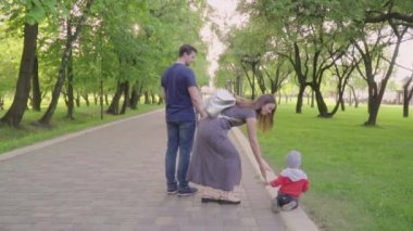 Güzel aile zevk yaz günü parkta: annem ve babam ilk adımlarını yapmak için ona yardım ile yürümeyi öğrenen küçük bebek