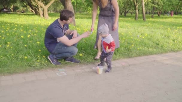 Niño pequeño con padres jóvenes pinta tiza sobre asfalto. Movimiento lento — Vídeos de Stock