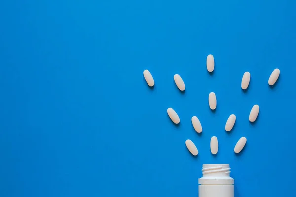 Witte Tabletten Verspreid Een Plastic Fles Een Blauwe Achtergrond — Stockfoto
