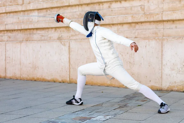 Portrait of man or woman in white fencing suit practicing with sword in the street.