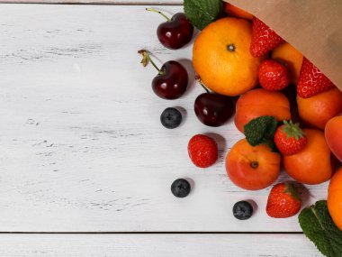 Tahta bir masada taze meyveler farklı meyveler ve böğürtlenler bir kese kağıdının içindeki ahşap masada yatıyor..