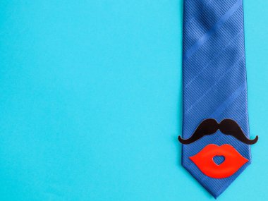 Mavi bir arka planda mavi kravat kağıt bıyıklı ve dudaklı mavi bir kravat mavi arka planda uzanıyor, üst taraf yakın plan, solda yazı için yer var..