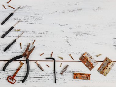 Beyaz ahşap arka plandaki aletler... pense, farklı boyutlardaki karanfiller, vidalar ve tornavidalar sol alt köşede, beyaz ahşap bir masada, yakın plan ve sağda yazı için yer var..