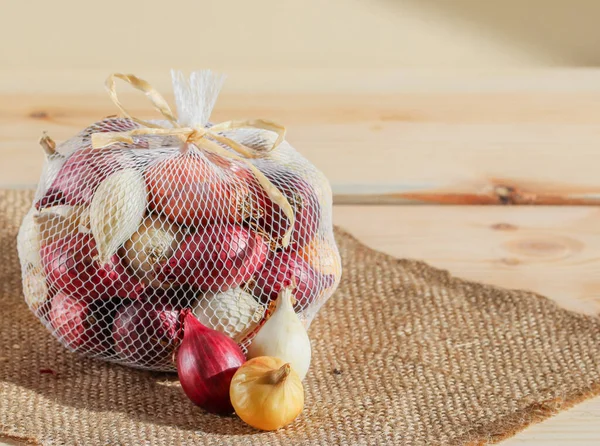 small onions of different varieties in a grid on a wooden table with a rustic burlap napkin. Close-up side view.