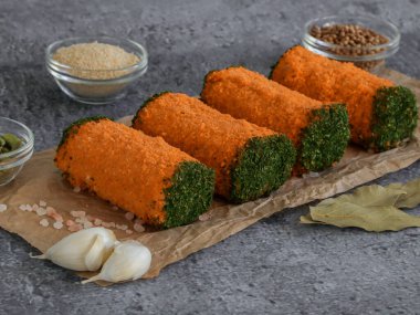 Parlak turuncu ekmek kırıntılarında üç kıymalı rulo ve taş bir arka planda yeşillikler, yakından yan görünüm..