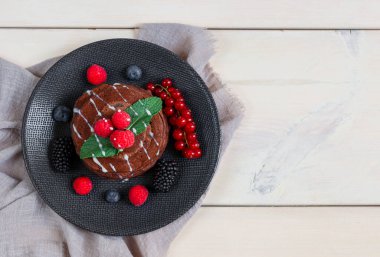 Üzerinde böğürtlen olan çikolatalı gözlemeler solda, tahta bir masada uzanıyor ve sağda yazı için yer var, en üstte yakın plan..