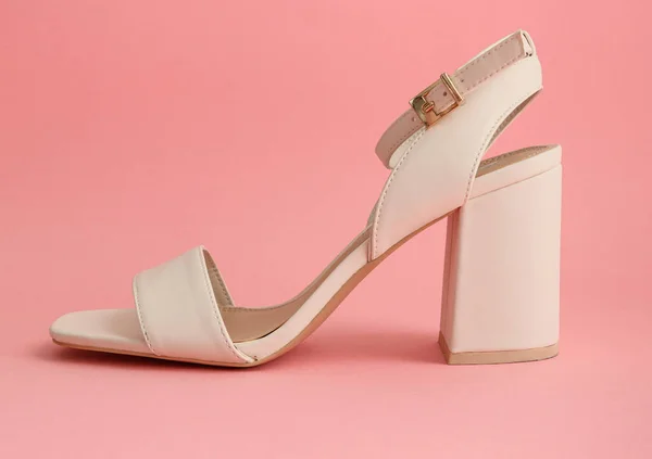 high heels shoesOne white sandal with high square heels stands on a pink background, close-up side view.