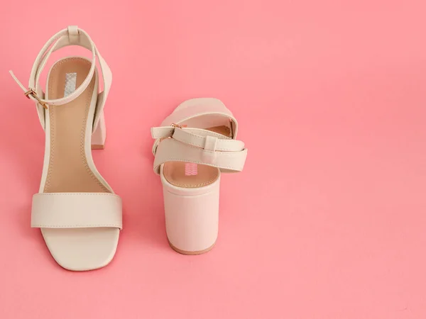 One pair of white sandals with high square heels stands against a pink background on the left and space for text on the right, close-up side view.