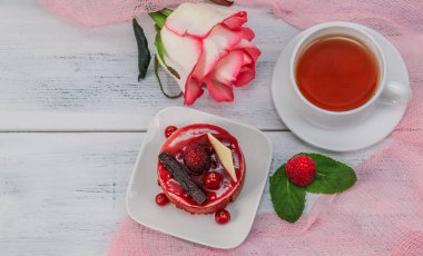 Bir kupa çayla ahududududulu kek ve beyaz ahşap bir masada pembe bir gül solda yazı için bir yer, en üstte yakın plan..
