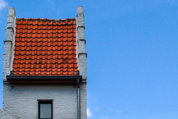 A red tile roof and a part of a white old building on the left against the sky and with space for text on the right, close-up side view.