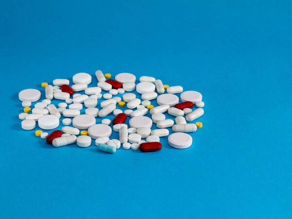 таблетки и капсулы........ Различные разноцветные таблетки и капсулы лежат в куче слева на синем фоне и с пространством для текста справа, вид сбоку крупным планом.