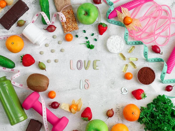 Fruits, food supplements and sports accessories....Fruits, nutritional supplements and sports accessories lie in a circle with the inscription love is in the center on a light cement background, close-up top view.