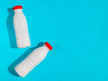 Solda kırmızı kapaklı iki beyaz plastik şişe var. Mavi zemin üzerinde sağda yazı için yer var. Tepeden yakın çekim görüntüsü..