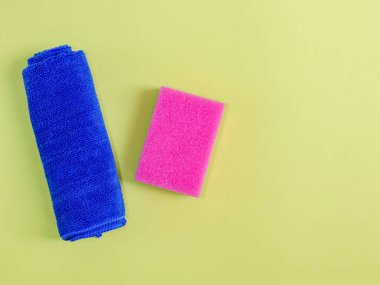 Mavi bir bez ve pembe bir temizlik süngeri sol tarafta sarı bir zemin üzerinde uzanıyor, sağda yazı için yer var, yakın çekim üst görünümü için..