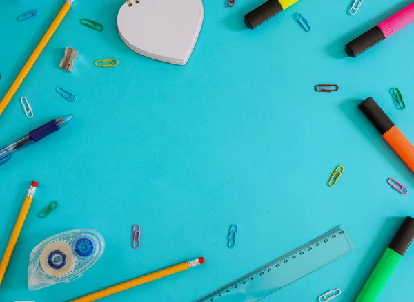 School supplies: markers, pencils, paper clips and more lie in a circle on a blue background with space for text in the middle, top view.