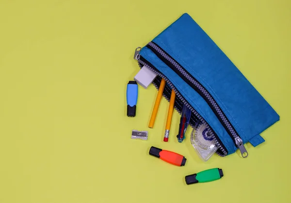A blue textile pencil case with pencils and markers lies on the right in the corner on a yellow background with space for text on the left, a close-up top view.