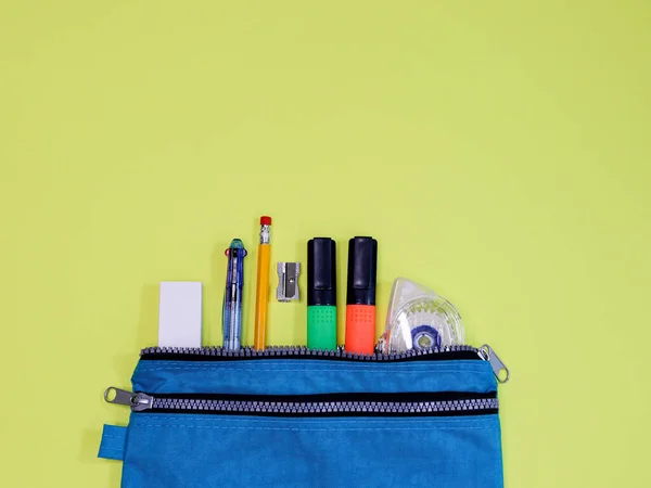 A blue pencil case with accessories lies in the middle from the bottom on a yellow paper background with a place for text on top, a close-up top view.