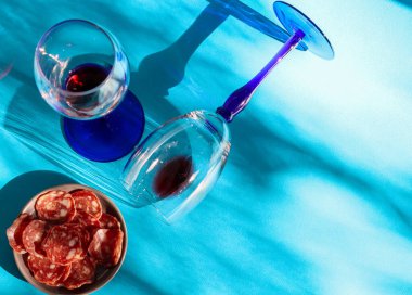 Kırmızı şaraplı iki bardak: biri yalan söylüyor ve diğeri solda güneşte kurutulmuş sosisle ayakta duruyor sağda yazı için yer var, üstte yakın çekim.