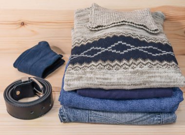 Kemerli ve çoraplı üst üste yığılmış kot pantolon ve kazaklar ahşap bir rafta, yakın plan yan görünüşte..