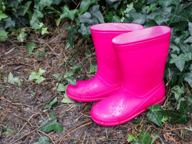 Bir çocuk için pembe lastik çizmeler sağda yağmurda yağmurda yatar solda yazı için yer, yakın çekim yan görüş.