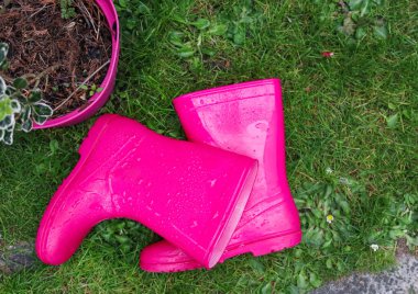 Yağmurdan sonra çimenlerin üzerinde solda yatan bir çocuk için pembe lastik çizmeler, sağda yazı için bir yer, yakın çekim üst görüş.