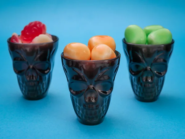 three skulls with candythree black skulls with colored halloween candies stand in a triangle on a blue background, close-up side view.