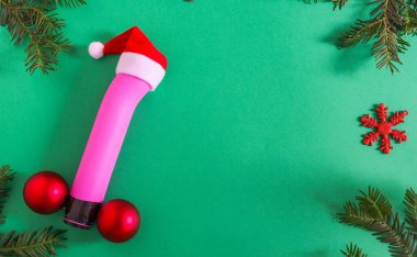 Pink dildo and christmas decorPink dildo in a Santa Claus hat and Christmas decor with a Christmas tree around the edges on a green background, top view close-up.