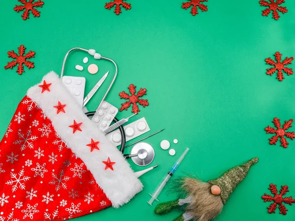 medical set with Santa Claus hatmedical set: stethoscope, pills and tools in a Santa Claus hat on the left on a green background with a place for text on the right, flat lay close-up.
