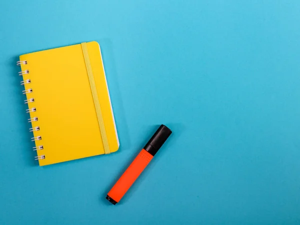 notepad and penA yellow notepad and an orange marker lie on the left against a blue background with space for text on the right, a close-up top view.