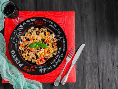 Farfalle makarna, çatal bıçak takımı, bir kadeh kırmızı şarap solda, siyah bir masanın üzerinde duruyor sağda yazı için yer var, üstten yakın çekim..