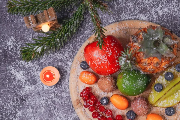 fruits on stone background      Tropical fruits with Christmas decor and snow lie on the right on a stone background, close-up top view.