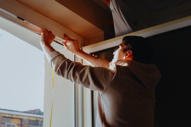 Genç, yakışıklı, esmer beyaz bir adamın portresi arkadan yan yana duruyor ve iki eliyle iç pencere çerçevesine özel kauçuk yapıştırıyor kışın çatlakları kapatmak için, yan görüş yakın plan. Onarım ve yalıtım konsepti