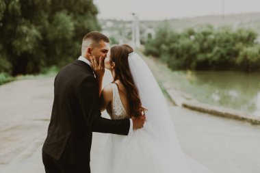 Güzel, şık, beyaz bir gelin ve damadın portresi. Bulanık bir yolda, yağmurlu bir günde, seçici bir odak noktasıyla birbirlerine sarılıp öpüşüyorlar..