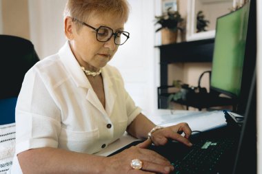Beyaz tenli güzel bir kadının yatay portresi. Ciddi bir kadın. Klavyesinde yeşil ekranla yazı yazıyor. Emeklilik yaşam tarzı konsepti, teknoloji kullanımı.