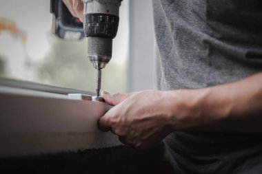 Kafkasyalı genç bir adam plastik pencere çerçevesi için matkapla metal tesisatlar kuruyor, tamiratın devam ettiği bir odada vidayı sıkıyor, aşağıdan seçici bir odak ile yakın çekim görüyor. Ev yenileme konsepti, pencere çerçeveleri.