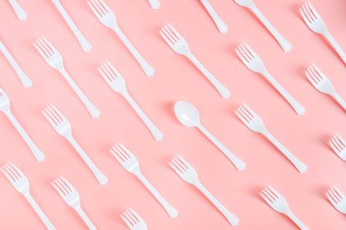 Birçok beyaz plastik çatal, tek kaşıkla açık pembe arka planda köşegen olarak yatar, düz yakın plan yatar. Ekoloji, plastik çöp ve tek kullanımlık plastik sofra takımı konsepti..
