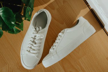 Güneşli bir günde, bir ev mağazasının kapısındaki hasır bir tencerede, lamine bir çiçekle birlikte, bir çift güzel, beyaz, klasik dantelli spor ayakkabı, tarlanın derinliği ile çok yakın bir şekilde yatar. Kadın ayakkabıları konsepti, ürün reklamcılığı..