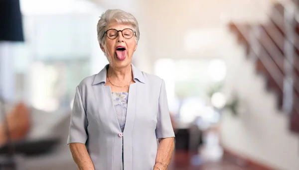 Beautiful senior woman expression of confidence and emotion, fun and friendly, showing tongue as a sign of play or fun at home.