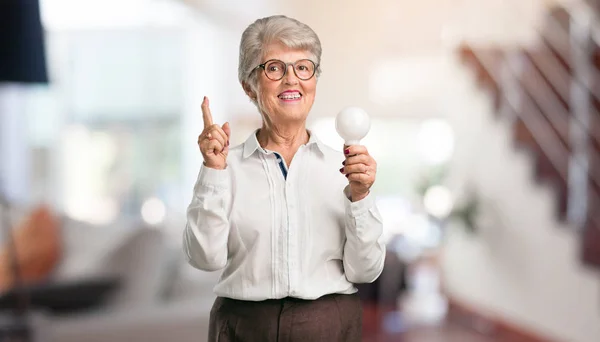 Beautiful Senior Woman Cheerful Excited Pointing Upwards Holding Light Bulb — Stock Photo, Image