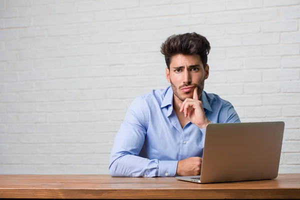 Jovem Homem Negócios Sentado Trabalhando Laptop Duvidoso Confuso Pensando Uma — Fotografia de Stock