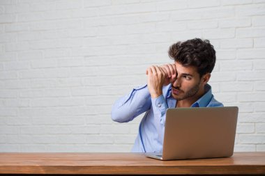 Gizleme ve şaşı oturan ve bir boşluk seyir bir dizüstü bilgisayar üzerinde çalışan genç iş adamı