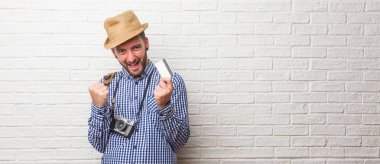 Silah yükselterek, bir zafer ya da başarı kutluyor, piyango kazanan sırt çantası ve bir vintage fotoğraf makinesi çok mutlu ve heyecanlı, giyen genç yolcusu adam. Bir kredi kartı tutan.